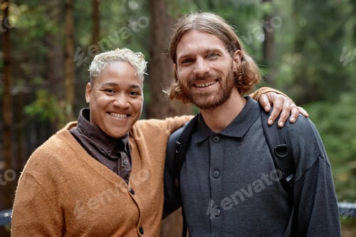 Preview: Portrait of multiethnic happy couple embracing and smiling at camera while walking in the forest