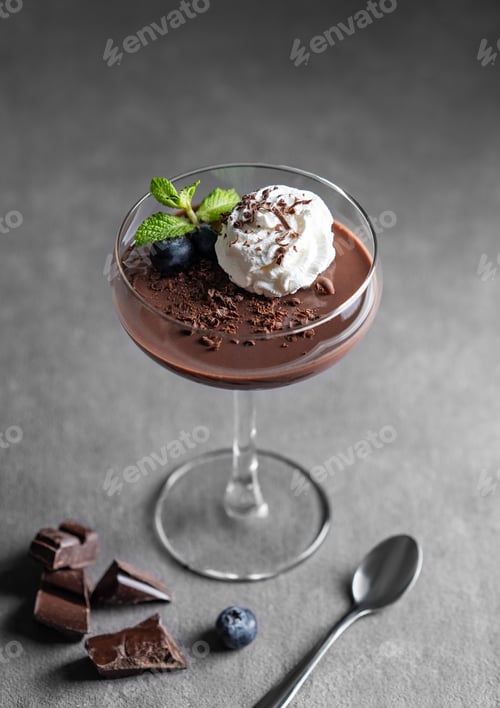 Preview: Chocolate pudding in a glass with whipped cream, fresh blueberries and mint on a dark background