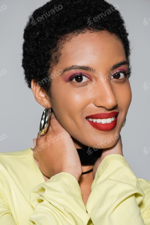 Preview: Carefree african american woman with makeup touching neck isolated on grey