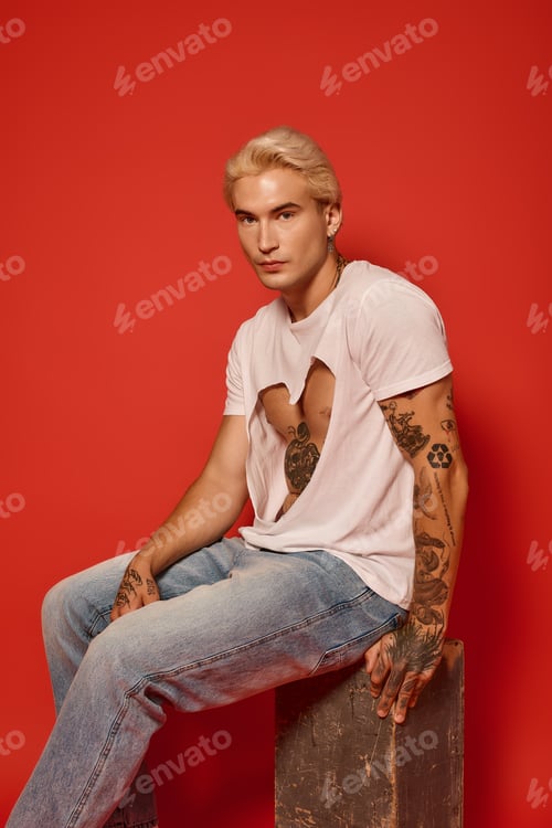 Preview: Stylish young man with tattoos posing confidently against a vibrant red background