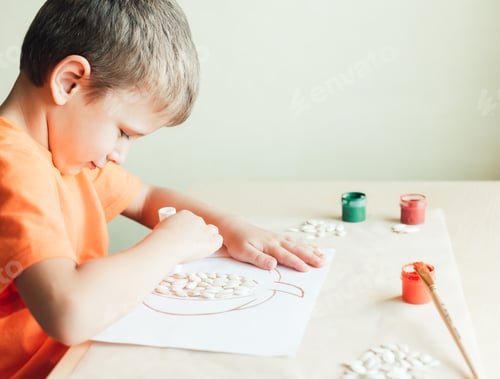 Preview: Cute boy making pumpkin from seeds on white paper, Halloween DIY concept