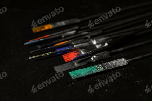 Preview: Tattoo needles covered with colorful inks on black background, closeup