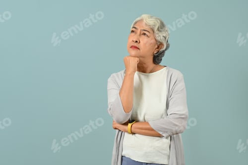 Preview: Thoughtful senior woman thinking and looking up expressing doubt and wonder isolated blue.