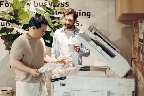 Preview: Businessmen discussing documents near photocopier in office