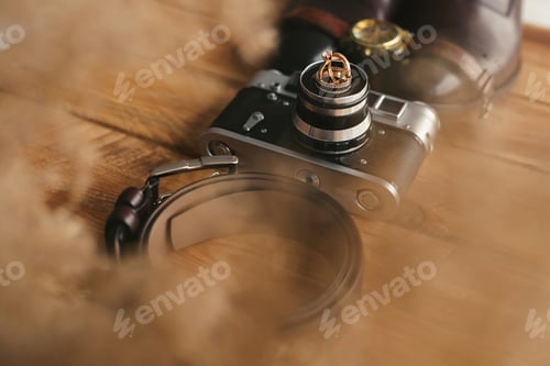 Preview: Wedding rings on an old camera, shoes, watch, and belt. Men's attributes on the wooden floor