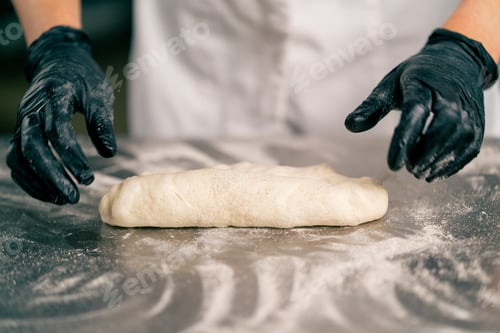 Preview: a chef's hands and dough lying in flour on a kitchen surface before forming a croissant shape