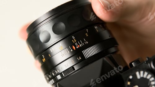Preview: Photographer hand changing manual aperture ring on the vintage film photo camera lens.