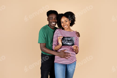 Preview: Smiling millennial african american husband hugging woman with big belly, show ultrasound scan