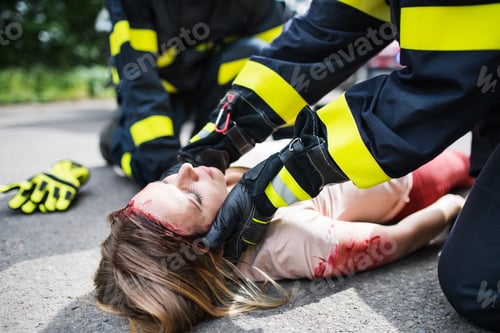 Preview: Unrecognizable firefighters helping a young injured woman lying on the road after an accident.