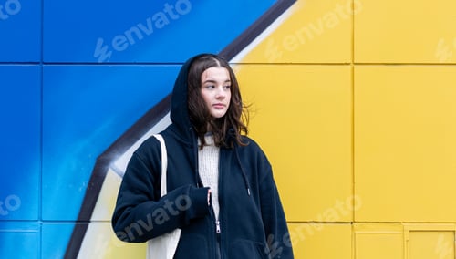 Preview: A young woman against a yellow-blue wall, urban graffiti.