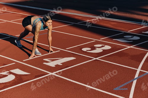Preview: Attractive girl in sportswear standing in starting position ready for running on city stadium