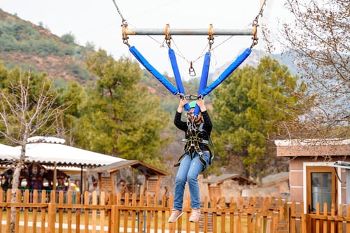 Preview: Teenage teen girl bungee flying in rope amusement park. Climbing harness equipment, green sports