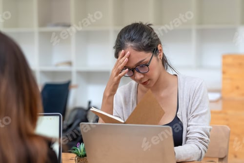 Preview: Front view of Asian businesswoman wearing glasses serious about the documents she holds at the offic