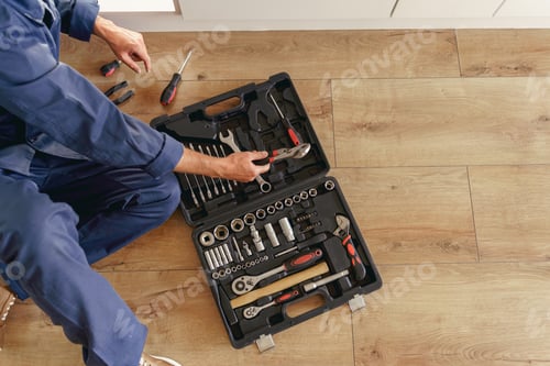 Preview: Top view of professional handyman with open tool bag sitting on home kitchen floor