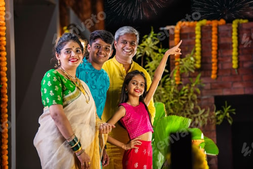Preview: Indian family celebrating Diwali, with a young girl pointing at fireworks in the night sky