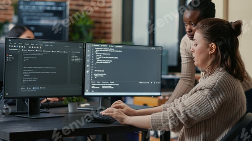 Preview: Junior programer writing algorithm under experienced colleague supervision sitting at desk with