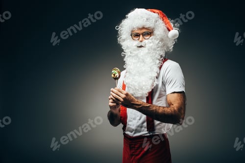 Preview: happy santa claus in eyeglasses standing with colorful lollipop isolated on grey background