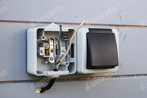 Preview: Outdoor socket installation in progress on light wooden wall shows exposed wires and open cover