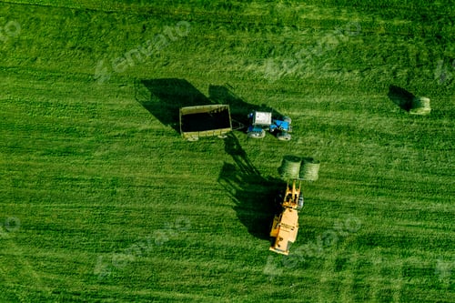 Preview: Aerial view of green grass harvest field with tractor moving hay bale