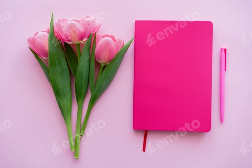 Preview: top view of tulips near notebook and pen on pink