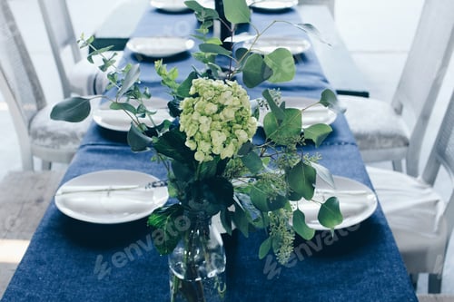 Preview: Horizontal shot of green and white flower centerpiece on table with the blue table cloth