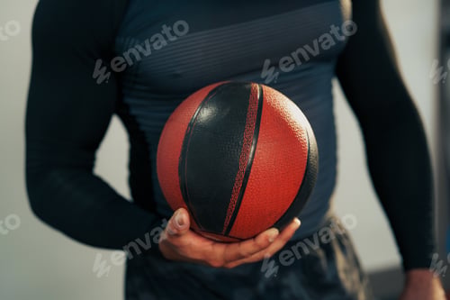 Preview: Smiling athlete holding a basketball indoors during a training session in a modern gym