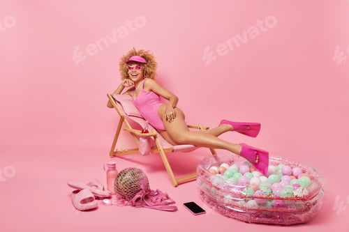 Preview: Happy relaxed woman lies on comfortable deck chair wears pink sunglasses swimsuit flippers spends su