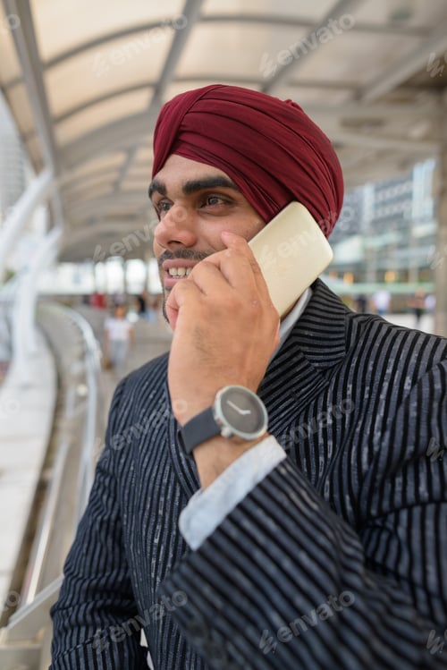 Preview: Indian businessman with turban outdoors in city talking on phone