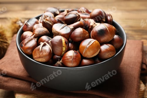 Preview: Delicious roasted edible chestnuts in bowl on table, closeup