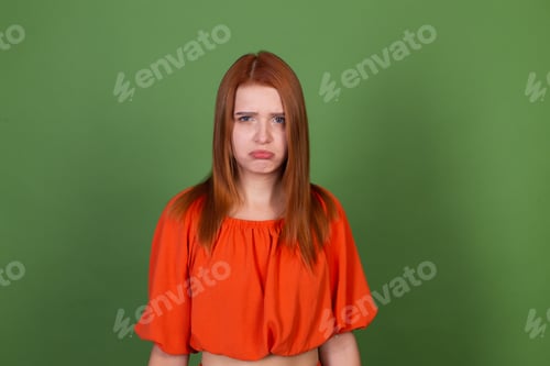 Preview: Young red hair woman in casual orange blouse on green background sad angry disappointed