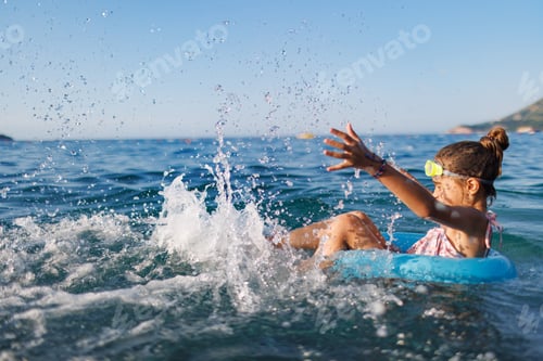 Preview: Cheerful girl sits in an inflatable circle and splashes with water in the sea
