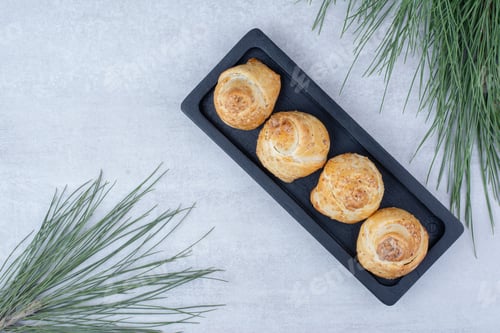 Preview: Baked sweet rolls on black plate with pine tree branch