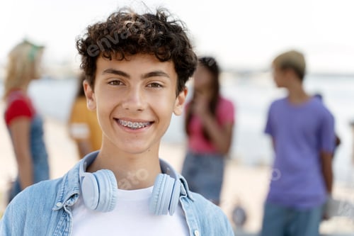 Preview: Portrait of smiling teenager with braces wearing headphones looking at camera standing on the street
