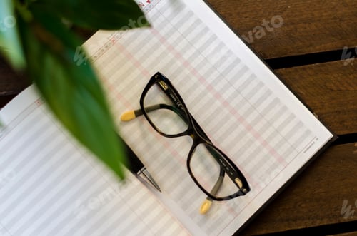 Preview: Eyeglasses on Open Planner on Wooden Desk