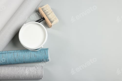 Preview: Different wallpaper rolls, brush and bucket with glue on light background, flat lay. Space for text