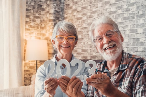 Preview: Portrait of couple of two old pensioners holding together numbers of 2023 at home