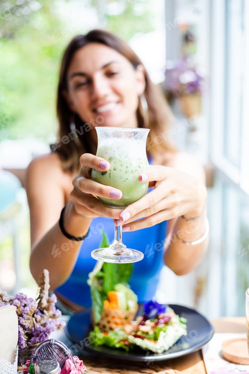 Preview: woman holds japanese matcha green tea with ice in glass in cafe