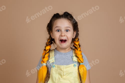 Preview: Little female having yellow kanekalon pigtails making grimace, looking at camera with shocked face