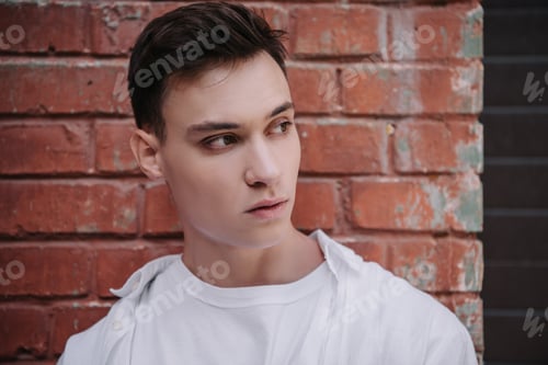 Preview: portrait of handsome young man looking away near brick wall