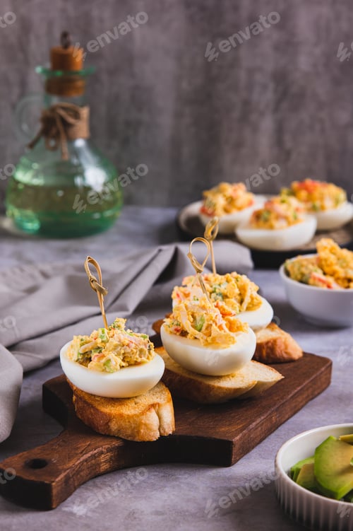Preview: Deviled eggs with tomatoes and avocado on toast on a board vertical view