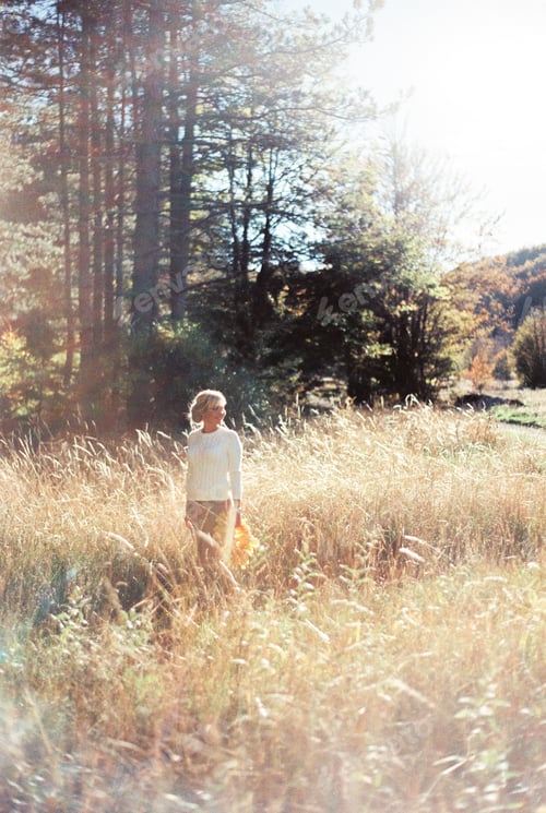 Preview: Woman with a wreath of yellow leaves stands among the dry grass on the lawn