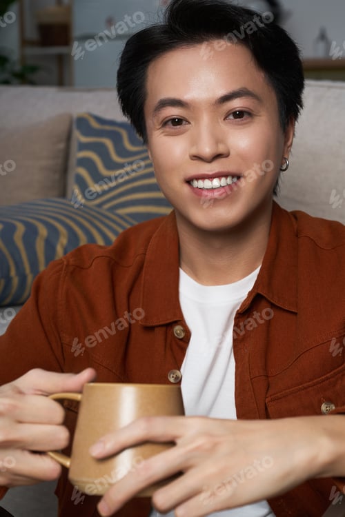 Preview: Young man enjoys a warm drink in his cozy modern apartment during a relaxing afternoon