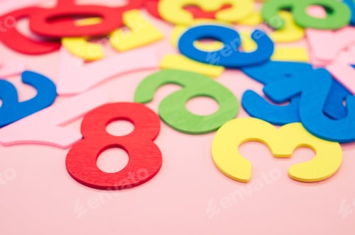 Preview: Closeup shot of the colorful wooden numbers scattered on a pink surface - space for text