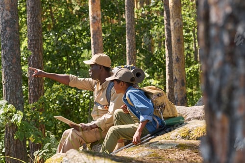 Preview: Confident senior man pointing forwards while sitting on stone next to grandson