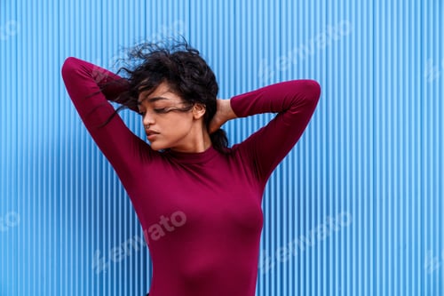 Preview: Young Brunette Caucasian Model Posing with Hands in Hair against Colorful Blue Wall, Copy Space