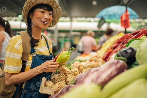 Preview: Asian woman in straw hat happily shops at vegetable stand farmers market
