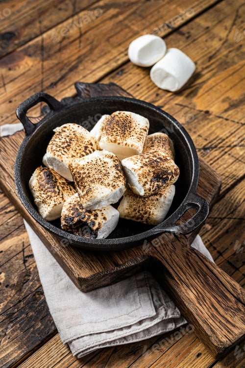 Preview: Toasted Marshmallow on open campfire in a skillet. Wooden background. Top view