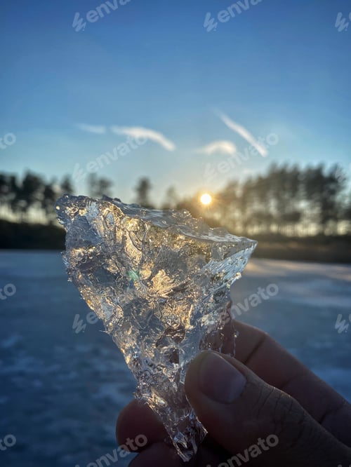 Preview: piece of ice in hand against the backdrop of the setting sun. rays of the sun in a piece of ice
