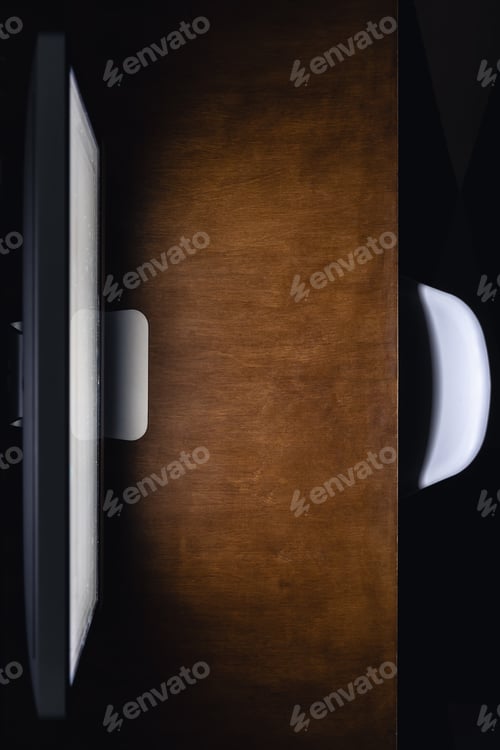 Preview: Computer monitor on a wooden table in a dark room, top view.