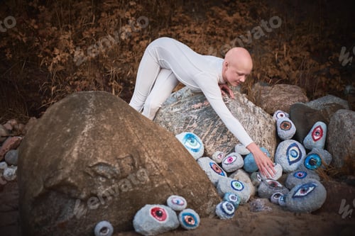 Preview: Young hairless girl with alopecia in white futuristic costume looking at surreal lot of rocks eyes